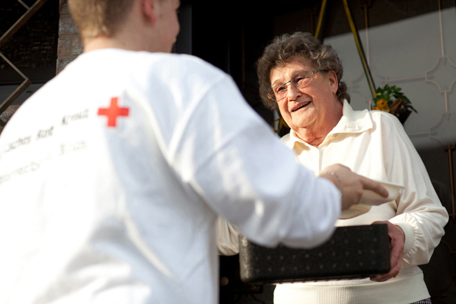 Ein Rotkreuz-Mitarbeiter übergibt einer Seniorin die Menüschale.