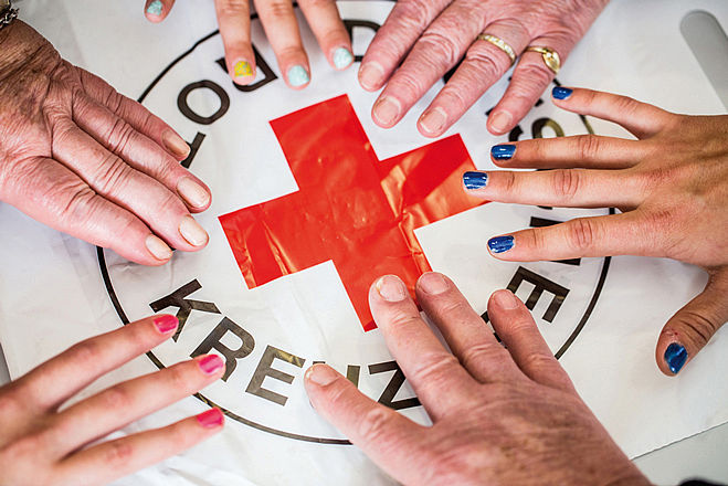 Bild zeigt Hände die zum Rotkreuz-Logo greifen.